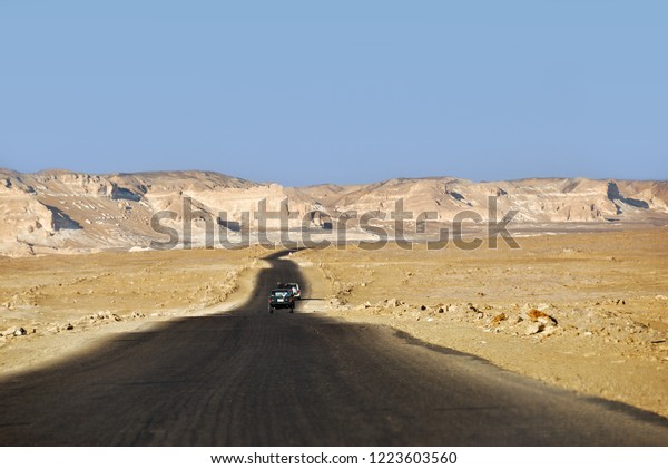 Tar road along sand dunes and sandstone\
rocks in Western desert between Farafra and Bahariya oasis. Sahara\
desert, Egypt, Africa. Selective focus on the\
car