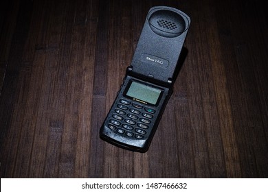 Taranto, Italy - 24 August 2019: Historic Motorola Startac Mobile Phone, Flip Open, Photographed On A Wooden Table Illuminated By A Single Light.