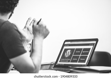 Taranto, Italy-July 19, 2019: laptop with WordPress logo on the monitor, in the foreground blurred the developer explains with pen in hand, free space on the right for text, monochrome image.