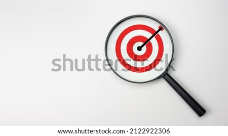 Target board inside of magnifier glass for focus business objective on white background and copy space. search and analysis of targets. Hand with magnifying glass holds its hand over target. wide
