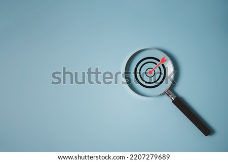Target board inside of magnifier glass for focus business objective achievement concept on blue background and copy space. Search, goal, strategy, success.