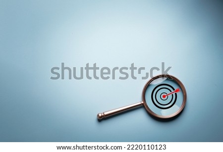 Target board inside of magnifier glass for focus business objective target search concept and success on blue background and copy space.