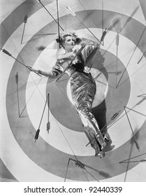 A target of desire, a young woman lying on the bulls eye with arrows around her