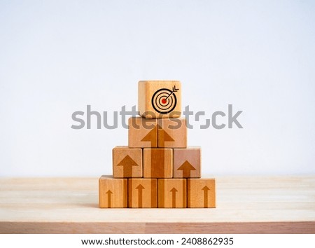 Target icon on top of wooden cube blocks stack as pyramid shape with rise up arrows on white background. Business goal process, Growth marketing, profit, investment, economic improvement concepts.