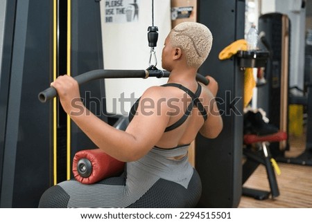 Target shoulder muscles with a pulldown machine: A fit-looking young black woman trains in the gym for strong shoulder muscles