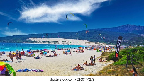 Tarifa, (Costa de la luz, Playa de Bolonia), Spain - June, 18. 2016: Beautiful natural crowded lagoon sand beach, kite surfers kitesurfing, dunes, green hill, blue sky 