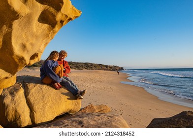 Tarifa, Spain - 05.01.2022: Couple sitting on a rock enjoying the view of a marvelous beach on the Atlantic coast of south Spain, near Tarifa