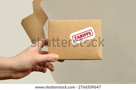 Tariffs concept, small labelled box in hand. Red and white tariff sticker, sign on cardboard box. Worldwide shopping, business taxes, trade war. Unfolded boxes as background