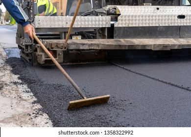 Tarmac Laying Machine At A Road Construction Site. Worker Leveling Fresh Asphalt On A Road Construction Site. Worker Using Asphalt Lute. 