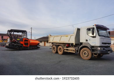 Tarn, France - Feb. 2021 - Construction Equipment For Road Works In A Parking Lot : A White, Six-wheeled Renault Tipper Truck In The Forefront, And A Volvo ABG Asphalt Paver In The Background