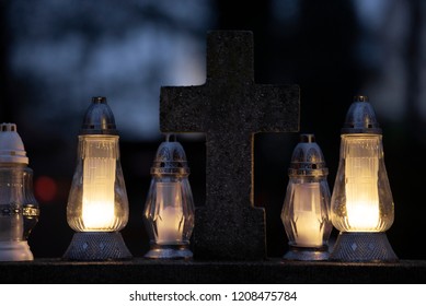 TARNOW, POLAND - NOVEMBER 01, 2017: Candles on the grave glowing in the dark around cross-relief.  All Saints Day  festival celebrated on a rainy day at the Old Cemetery, one of the oldest in Poland. 