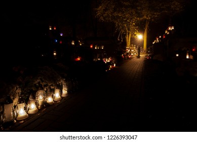 TARNOW, POLAND - NOVEMBER 02, 2018: A Lonely Person After Dark At The End Of The Alley Illuminated Only By The Light And Candles Praying At The Grave On The Old Cemetery.