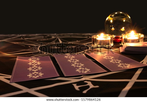 Tarot
cards on  table with a crystal ball and burning candles in the
background.Tarot reader or Fortune teller reading  tarot cards and
forecasting concept.Mystic and darkness
background.