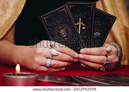 Tarot reader or Fortune teller of hands holding up black deck tarot cards. Tarot cards are spread on a table near burning candles. Forecasting concept.