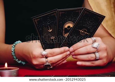 Tarot reader or Fortune teller of hands holding up black deck tarot cards. Tarot cards are spread on a table near burning candles. Forecasting concept.