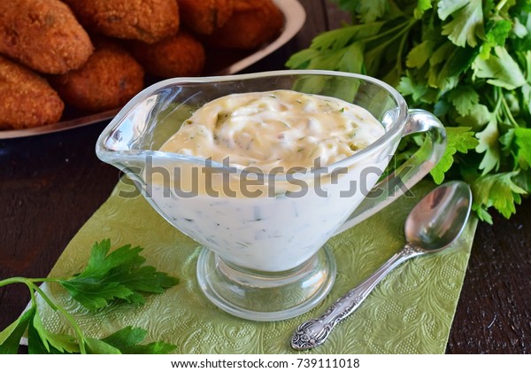 Tartar sauce for fish dishes with\
yogurt, capers, garlic and lemon, olive oil and sugar in a glass\
gravy boat on a dark wooden background. Healthy eating\
concept