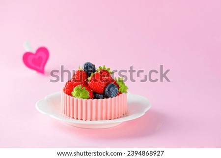 Tartlet or cake with strawberries, raspberries, blueberries and a basket of pink chocolate in a plate and heart on a pink background. Cake baskets with delicate cream and berries.