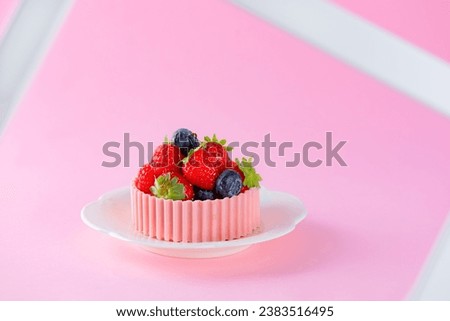 Tartlet with strawberries, raspberries, blueberries and a basket of pink chocolate on a pink background. Cake baskets with delicate cream and berries.