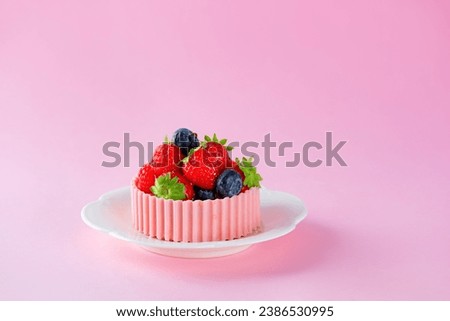 Tartlet with strawberries, raspberries, blueberries, basket of pink chocolate in a plate on a pink background. Cake baskets with cream and berries.