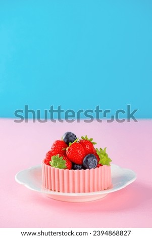 Tartlet with strawberries, raspberries, blueberries and a basket of pink chocolate in a plate on a blue and pink background. Cake baskets with delicate cream and berries. Vertical orientation.