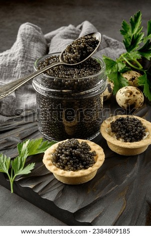 Tartlets with black Sturgeon caviar on wooden board. Caviar sandwiches and caviar in a Glass jar on a cutting Board. Bowl with black caviar. Black background.  Copy space
