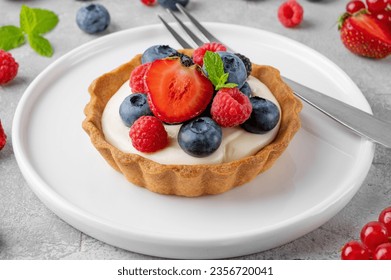 Tartlets with custard vanilla cream with fresh berries and mint on a gray concrete background. Summer dessert