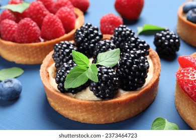 Tartlets with different fresh berries and mint on blue table, closeup. Delicious dessert - Powered by Shutterstock