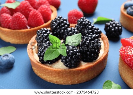 Tartlets with different fresh berries and mint on blue table, closeup. Delicious dessert