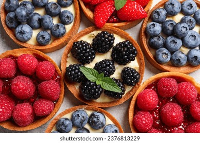 Tartlets with different fresh berries on light table, flat lay. Delicious dessert