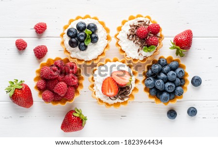 Tartlets (tarts, open pastry pies) with ricotta cheese (cottage cheese) and fresh berries (straberry, raspberry and blueberry). Healthy dessert breakfast, snack, morning table. White wooden background