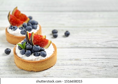 Tarts with blueberries and figs on white wooden table, space for text. Delicious pastries