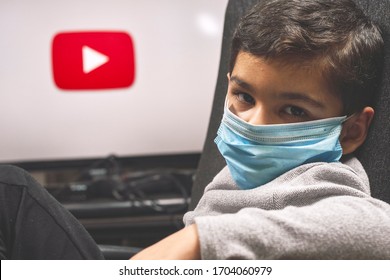 Tashkent, Uzbekistan - 26 March 2020: A Little Boy Watching Youtube During Coronavirus Self-quarantine. A Kid In Protective Medical Gloves Holds Remote Control And Watches TV