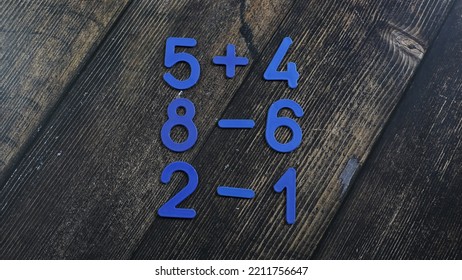 Task In Mathematics. Mathematics Problem For Children. Simple Algebra Examples Using Numbers And Signs From Plastic Numbers On A Wooden Background.