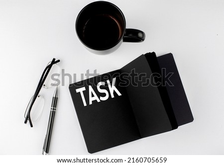 TASK written text in small black notebook with coffee , pen and glasess on a white background. Black-white style