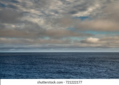 Tasman Sea, Australia - March 20, 2017: Lower Third Of Photo Is Blue Sea Water With Low Hanging Brown And Higher Floating White Clouds. Some Blue Patches Of Sky.