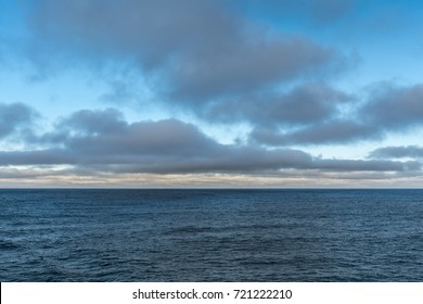 Tasman Sea, Australia - March 20, 2017: Lower Third Of Photo Is Blue Sea Water With Low Hanging Brown Clouds On The Horizon And Higher Floating Gray Clouds. Dispersed Blue Patches Of Sky.