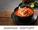 Taste of Thailand: Spicy and Sour Thai Tom Yum Goong Soup with Shrimp and Aromatic Ingredients on Black and Wooden Background