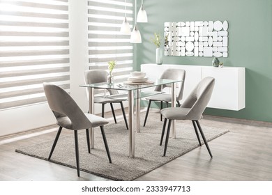 A tastefully appointed modern dining room with a glass table and chairs, situated in front of a large window with the grey blinds pulled up