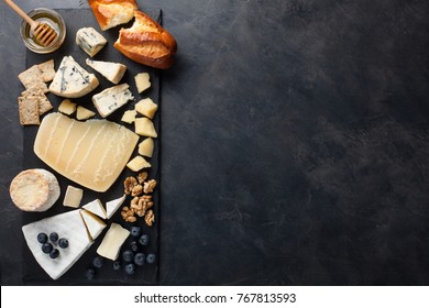 Tasting cheese dish on a dark stone plate. Food for wine and romantic date, cheese delicatessen on a black concrete background. Top view with copy space.