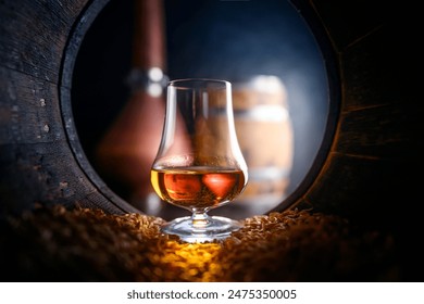 Tasting glass with whiskey standing inside of old oak barrel filled with barley grains. Traditional alcohol distillery concept