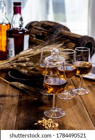 Tasting Glasses With Aged Scotch Whisky Or American Bourbon On Old Dark Wooden Vintage Table With Barley Grains