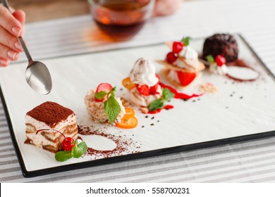 Tasting one cake from lots, close-up. Plate with five different sweet desserts, hand taking one. Degustation, choosing dessert for party or wedding, gastronomy, event organization concept