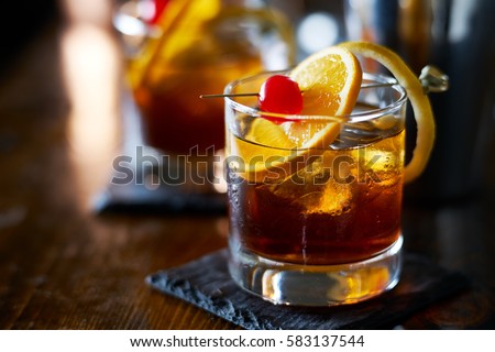 tasty alcoholic old fashioned cocktail with orange slice, cherry, and lemon peel garnish