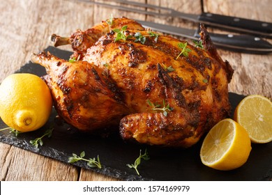 Tasty aromatic rotisserie chicken with thyme, lemon and spices close-up on a slate board on the table. horizontal
