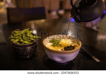Tasty Asian classic soup with noodles and meat. Fresh traditional food, vegetables noodle, gourmet food, best delicious cuisine, dark restaurant table closeup of bowl, hot water pouring onto noodles