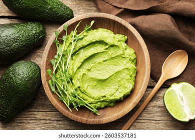 Sabrosa salsa de aguacate en un tazón, microverduras, lima y cuchara en la mesa de madera, plana