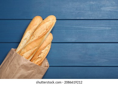 Tasty baguettes in package on blue wooden table, top view. Space for text