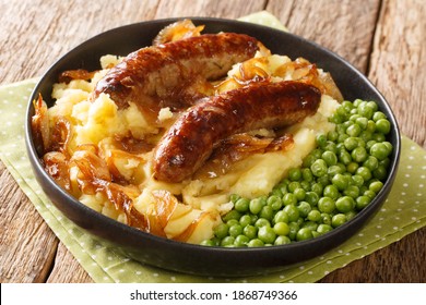 Tasty Bangers and Mash made of sausages served with mashed potatoes, green peas and onion gravy close-up in a plate on the table. Horizontal