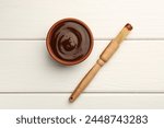 Tasty barbeque sauce in bowl and brush on white wooden table, top view