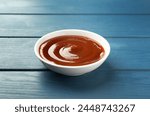Tasty barbeque sauce in bowl on blue wooden table
